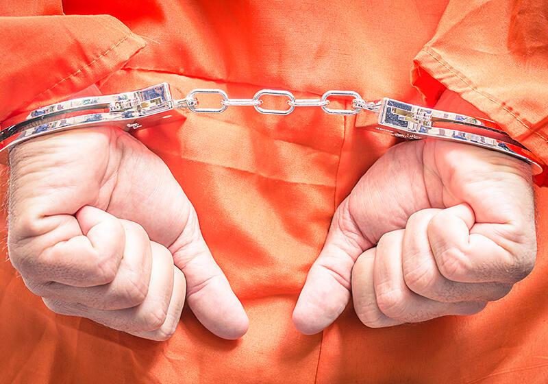 Hands in handcuffs behind the back of someone wearing an orange jumpsuit