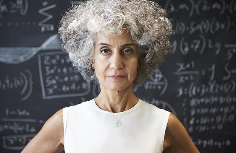 Female mathematician stares at camera in front of blackboard full of mathematical equations