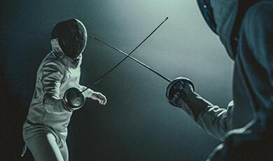 Two fencers face each other swords drawn