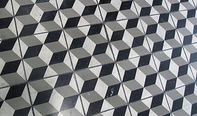 A close-up view of a floor tiled with a black, white, and gray geometric pattern creating a 3D cubic illusion