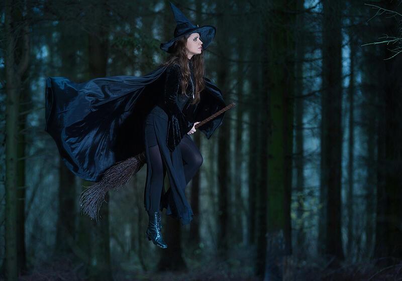 a woman dressed as a witch riding a broomstick in the woods