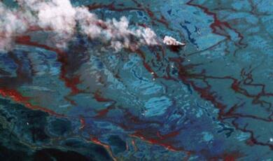 Aerial view of a controlled burn of an oil slick on a body of water, with smoke rising from the burning oil