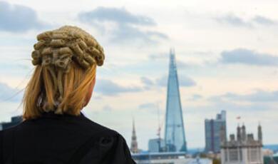 A person with blonde hair seen from behind, looking out a window at The Shard skyscraper in London