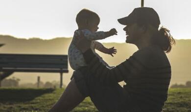 Photo of a man holding a baby and sitting on grass