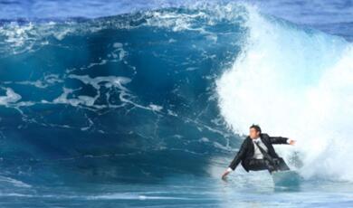 man in a suit riding a wave on a surfboard