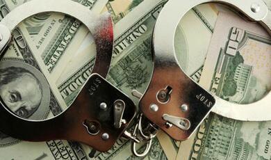 a pair of handcuffs placed on a bed of notes of american dollars