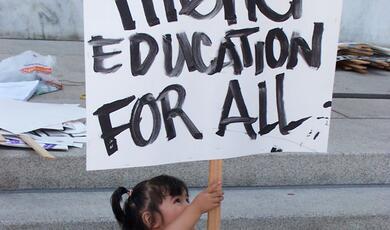 a child holding a placard with the words 'Higher Education For All' written on it