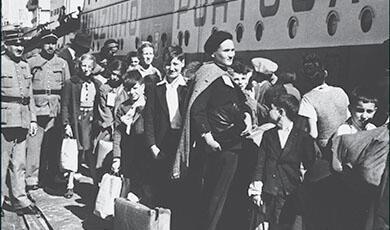 Two uniformed Portuguese policemen stand on the pier in the port of Lisbon as a group of Jewish refugee children wait in line to board the SS Mouzinho