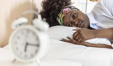 Tired lady lying down staring at back of alarm clock
