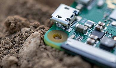 A close-up of a Raspberry Pi 4 circuit board partially buried in soil